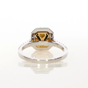May include: A white gold engagement ring with a yellow diamond center stone and a halo of smaller diamonds. The ring has a pave setting and a band that is adorned with smaller diamonds.