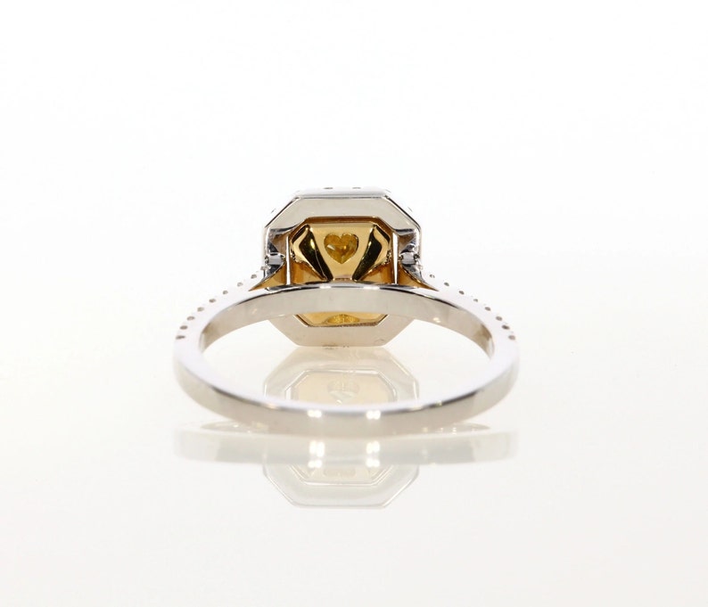 May include: A white gold engagement ring with a yellow diamond center stone and a halo of smaller diamonds. The ring has a pave setting and a band that is adorned with smaller diamonds.