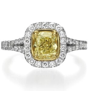 May include: A yellow diamond engagement ring with a halo setting and a double band. The ring is set in white gold and features a cushion-cut diamond.