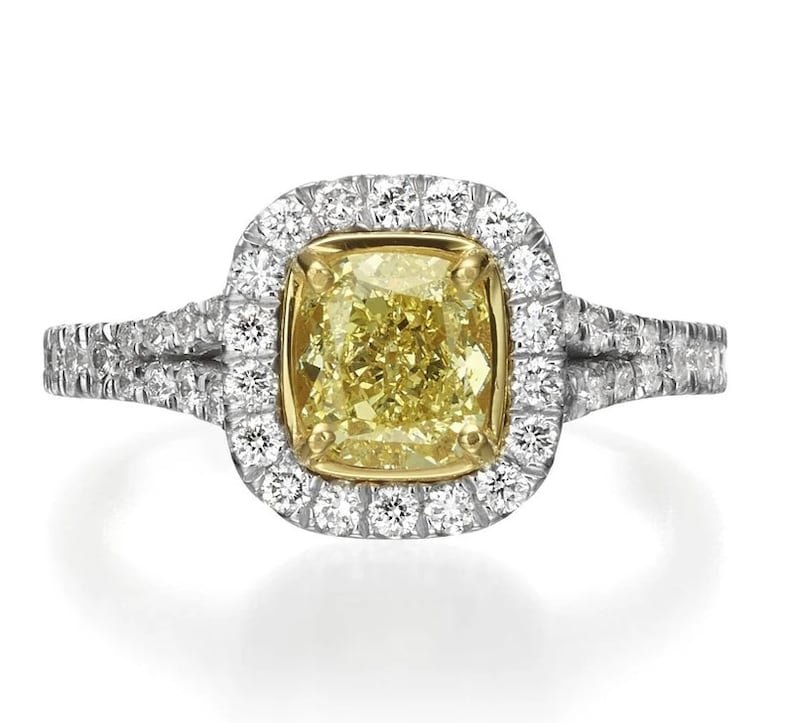 May include: A yellow diamond engagement ring with a halo setting and a double band. The ring is set in white gold and features a cushion-cut diamond.