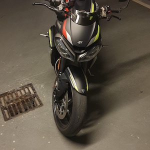 Może przedstawiać: Czarny motocykl z ż&oacute;łtymi i czerwonymi akcentami. Motocykl ma czarne siedzenie i czarną szybę. Motocykl jest zaparkowany w garażu.