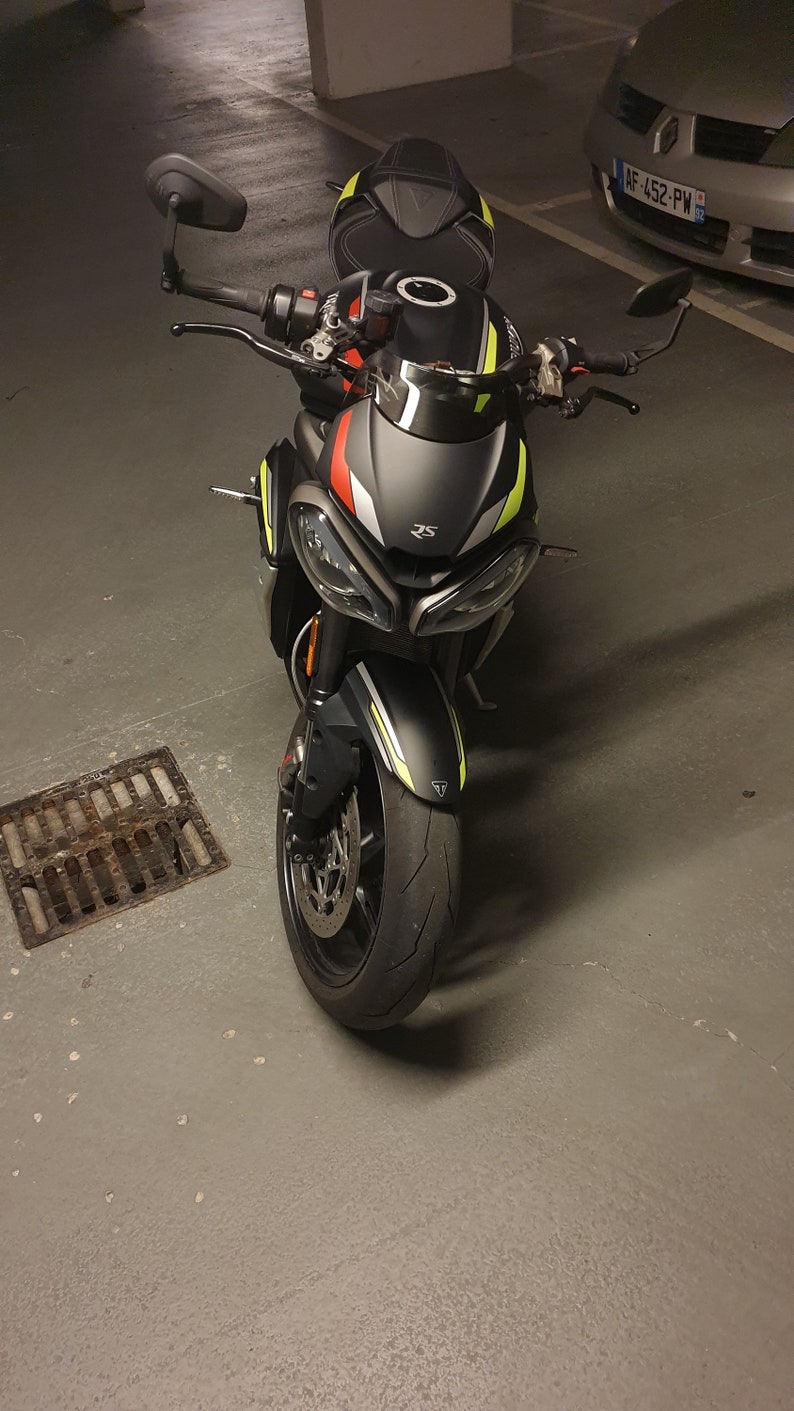 Może przedstawiać: Czarny motocykl z ż&oacute;łtymi i czerwonymi akcentami. Motocykl ma czarne siedzenie i czarną szybę. Motocykl jest zaparkowany w garażu.
