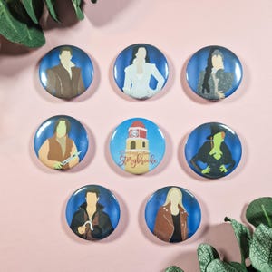 May include: Set of eight 1-inch button badges featuring characters and a landmark from the TV show Once Upon a Time. The badges are round and have a blue background with white outlines. The characters include Snow White, Prince Charming, Captain Hook, Regina, Rumpelstiltskin, and the Evil Queen. The landmark is the clock tower in Storybrooke.