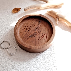 Puede incluir: Una bandeja redonda de madera con un acabado marr&oacute;n oscuro. La bandeja tiene un dise&ntilde;o floral y las iniciales "WB" grabadas en ella.