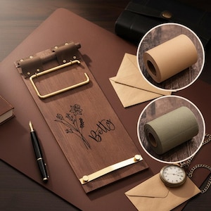 May include: A wooden clipboard with gold-colored hardware and the name "Betty" engraved on it, along with a floral design. The image also includes a black pen, rolls of paper, envelopes, and a pocket watch.