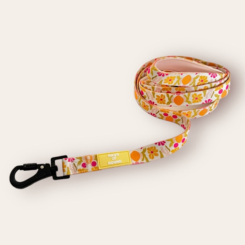 May include: A white, pink and yellow floral patterned dog lead with a yellow label that reads "Haus of Hound".