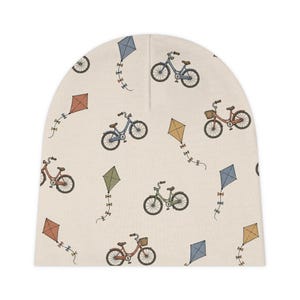 Könnte beinhalten: Beige Baby-Beanie mit einem sich wiederholenden Muster aus Fahrrädern und Drachen in verschiedenen Farben. Die Fahrräder sind blau, grün und rot, und die Drachen sind orange, gelb und blau.