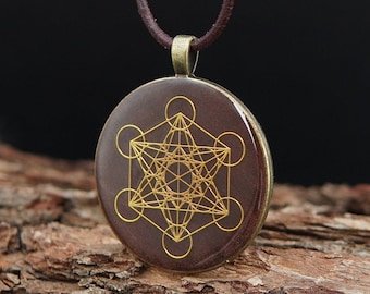 Op de afbeelding: Een bruine ketting met een ronde hanger met een gouden geometrisch ontwerp. De hanger heeft een complex patroon van lijnen en cirkels.