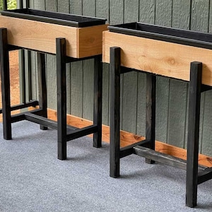 Può includere: Due fioriere in legno con supporti in metallo nero. Le fioriere sono in legno chiaro e i supporti sono neri.