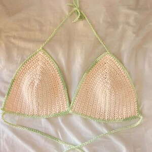 May include: A crocheted halter top with a light pink base and a light green trim. The top has adjustable straps and ties at the back.