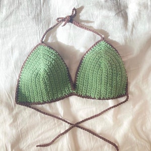 May include: A green crocheted bikini top with brown straps. The top is made with a simple stitch and has a triangular shape.