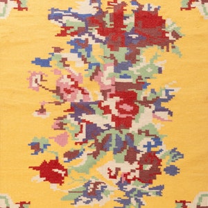 K&ouml;nnte beinhalten: Ein gelber Teppich mit einem floralen Muster in Rot-, Blau-, Gr&uuml;n- und Rosat&ouml;nen. Der Teppich hat einen Fransenrand.