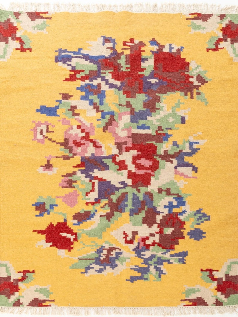 K&ouml;nnte beinhalten: Ein gelber Teppich mit einem floralen Muster in Rot-, Blau-, Gr&uuml;n- und Rosat&ouml;nen. Der Teppich hat einen Fransenrand.