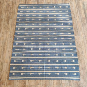 Op de afbeelding: Een blauw en wit gestreept tapijt met een geometrisch patroon. Het tapijt is gemaakt van katoen en heeft een zachte, comfortabele textuur.