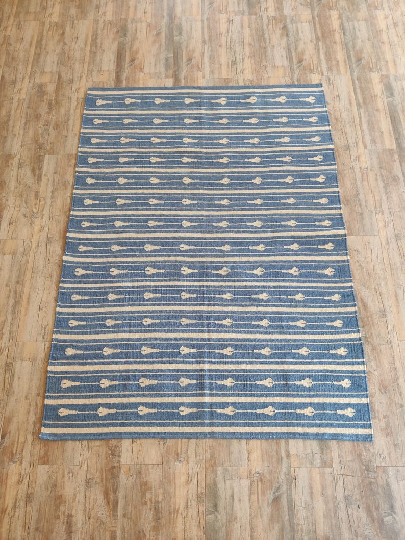 Op de afbeelding: Een blauw en wit gestreept tapijt met een geometrisch patroon. Het tapijt is gemaakt van katoen en heeft een zachte, comfortabele textuur.