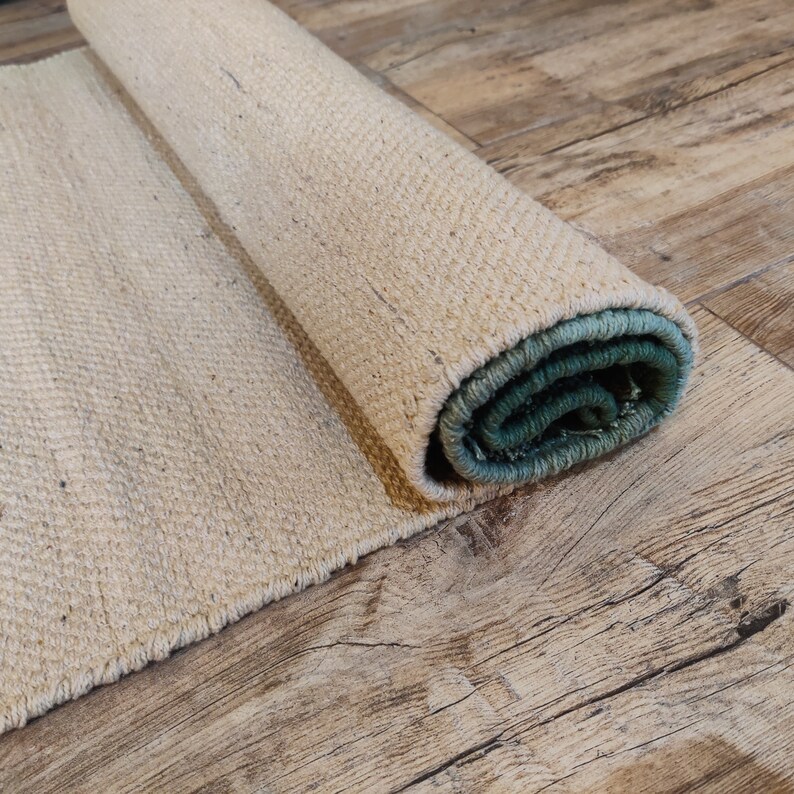May include: A rolled-up natural fiber rug with a green and blue border. The rug is lying on a wooden floor.
