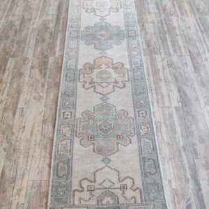 May include: A vintage runner rug with a light beige background and a repeating pattern of green, pink, and brown floral motifs. The rug has a fringed edge.