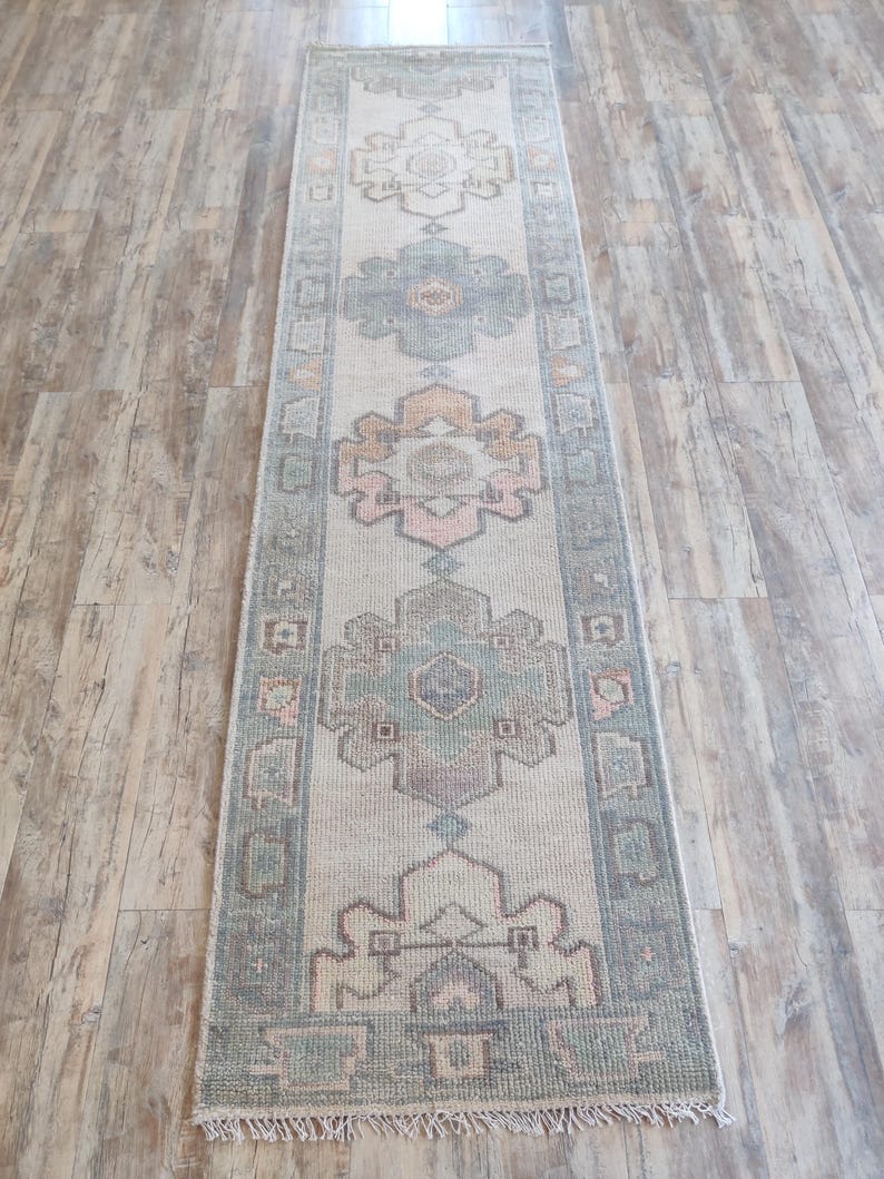 May include: A vintage runner rug with a light beige background and a repeating pattern of green, pink, and brown floral motifs. The rug has a fringed edge.