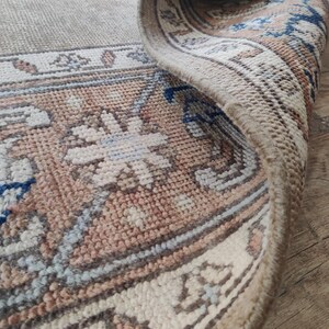 May include: Close-up of the edge of a beige rug with a floral pattern. The rug has a fringe border and is woven with a variety of colors, including beige, brown, blue, and white.