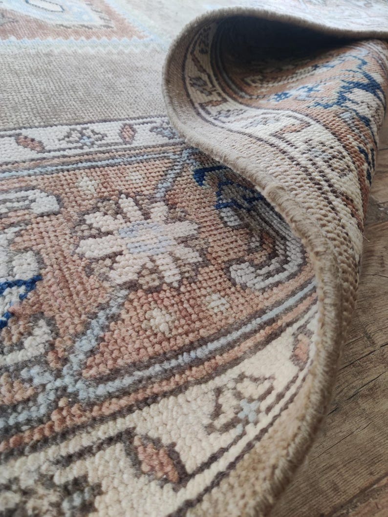 May include: Close-up of the edge of a beige rug with a floral pattern. The rug has a fringe border and is woven with a variety of colors, including beige, brown, blue, and white.
