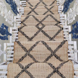 May include: A natural fiber rug with a diamond pattern in black and beige. The rug has a fringe border and is laid out on a set of stairs.