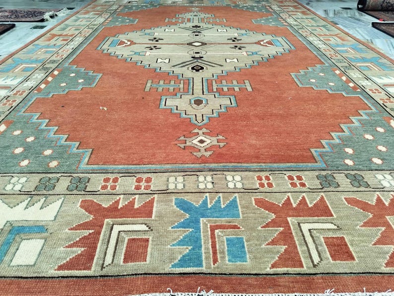 An angled view of a handcrafted rust-burnt orange Oushak rug with soft, muted wool texture and intricate geometric border patterns for a contemporary, traditional home
