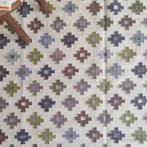 May include: A white rug with a geometric pattern in shades of green, brown, and blue. The pattern is made up of small squares and diamonds.