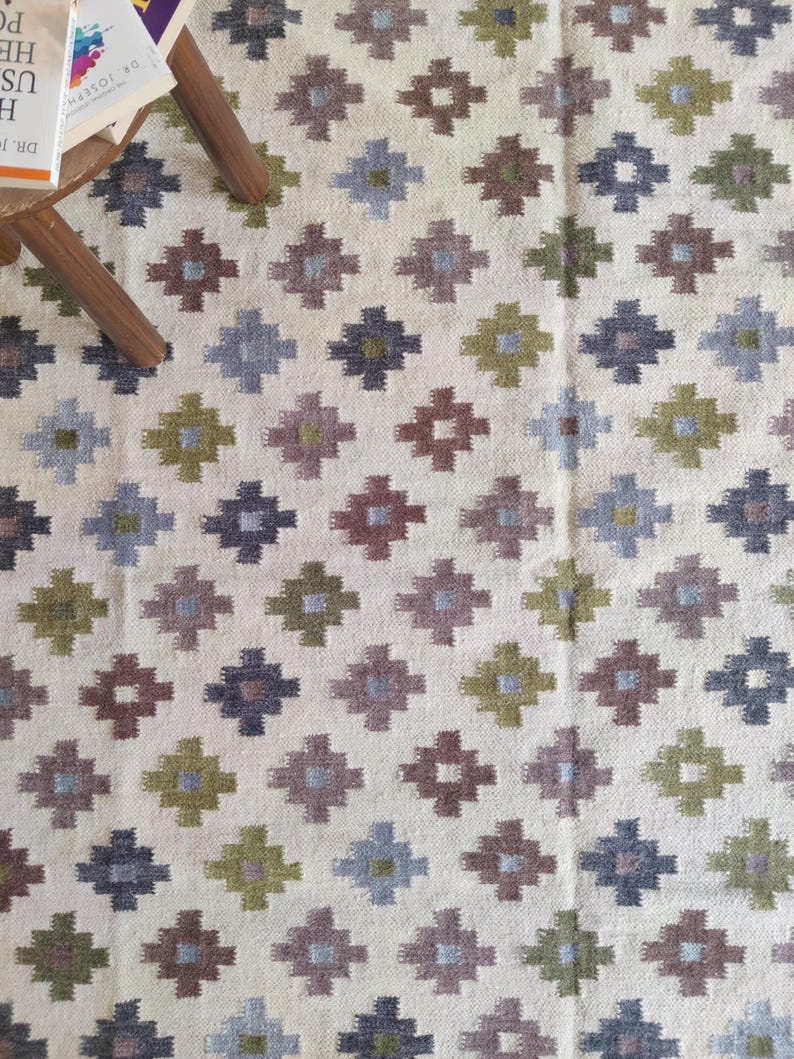 May include: A white rug with a geometric pattern in shades of green, brown, and blue. The pattern is made up of small squares and diamonds.