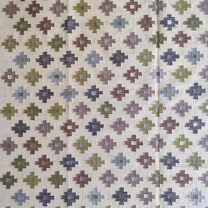 May include: A white rug with a geometric pattern of brown, green, blue, and gray diamonds. The rug has a woven texture.