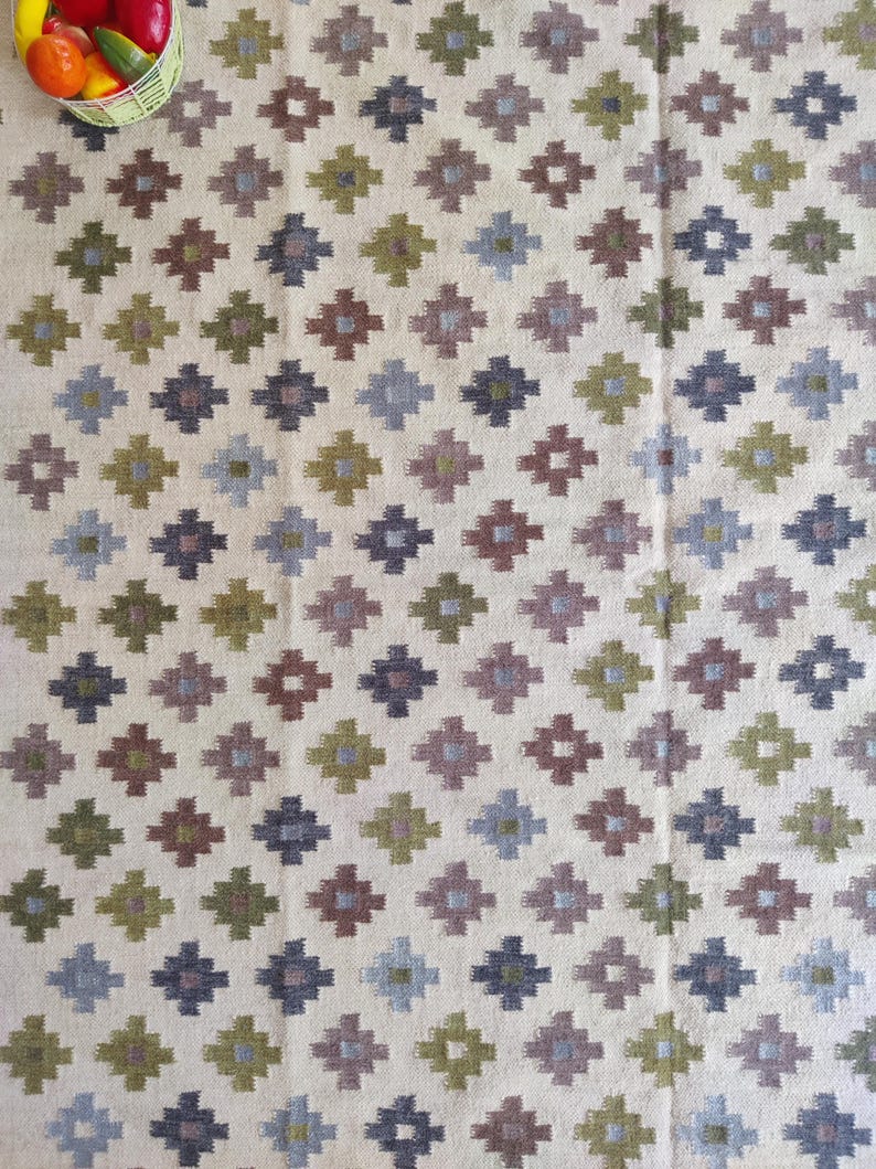 May include: A white rug with a geometric pattern of brown, green, blue, and gray diamonds. The rug has a woven texture.