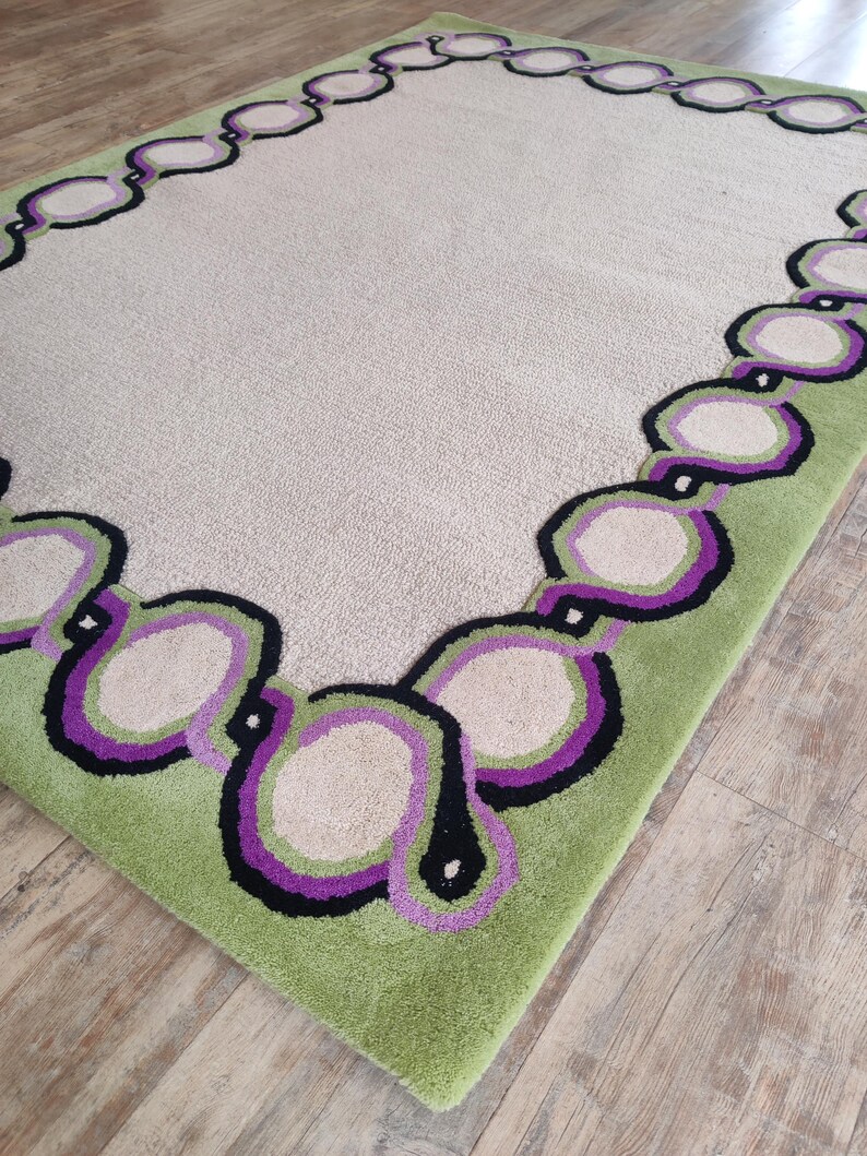 Hand tufted wool rug with green border and purple chain pattern on neutral background, modern designer area rug for living room or bedroom