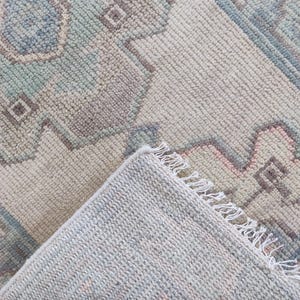 May include: A light blue and cream coloured rug with a geometric pattern. The rug has a fringe border and is folded in half.