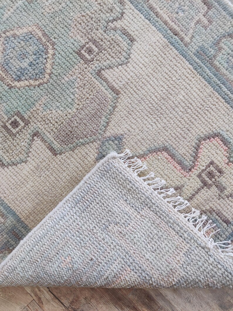 May include: A light blue and cream coloured rug with a geometric pattern. The rug has a fringe border and is folded in half.