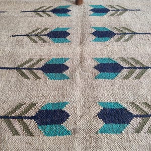 May include: A beige rug with a repeating pattern of blue and green arrows. The rug is woven with a textured surface.