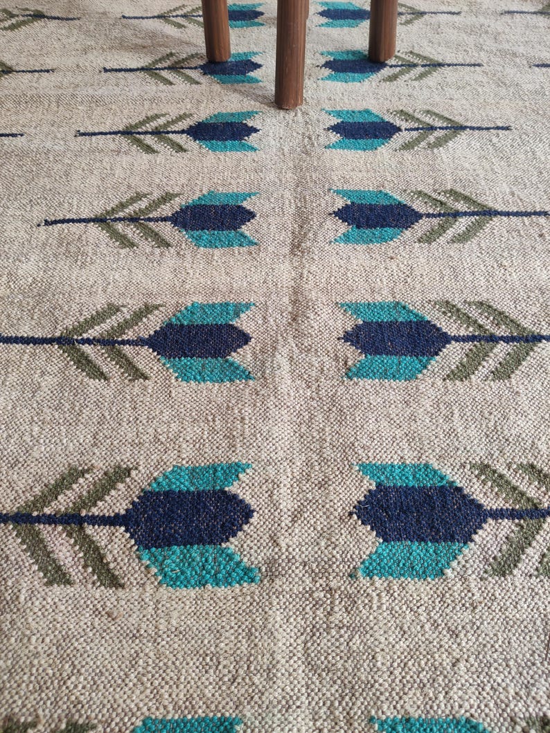 May include: A beige rug with a repeating pattern of blue and green arrows. The rug is woven with a textured surface.