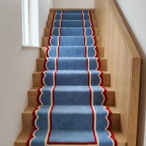 May include: A staircase with light blue carpet runners. The runners have a scalloped edge with a red border and a white inner stripe. The stairs are made of light-colored wood.