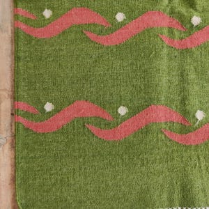 May include: Green rug with a fringed border and a repeating pattern of pink wavy lines with white dots.