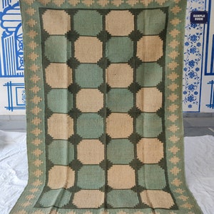 May include: A green and beige woven rug with a geometric pattern. The rug has a fringe border.