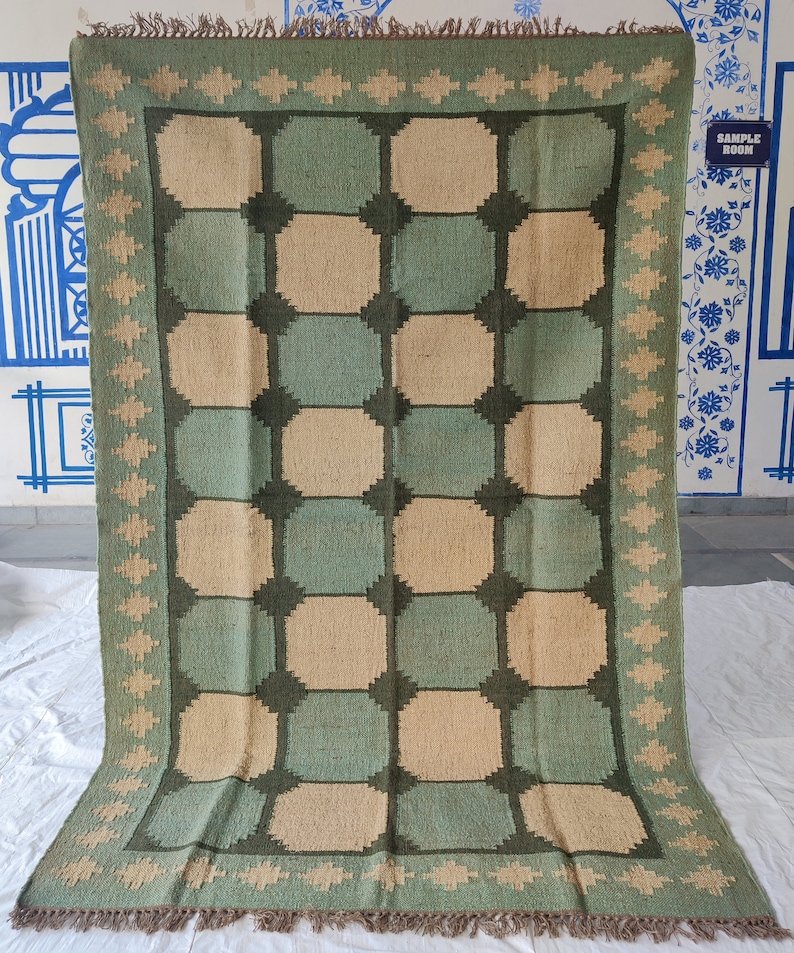 May include: A green and beige woven rug with a geometric pattern. The rug has a fringe border.