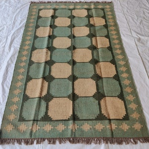 May include: A green and beige patterned rug with a geometric design. The rug has a fringe border.