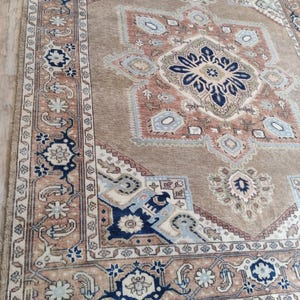 May include: A beige rug with a large, intricate, multi-colored design. The rug has a border with a floral pattern and a fringe.