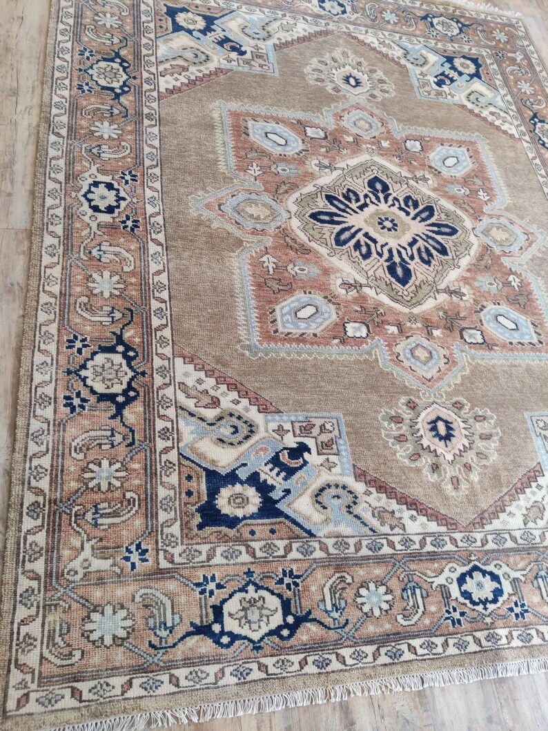May include: A beige rug with a large, intricate, multi-colored design. The rug has a border with a floral pattern and a fringe.
