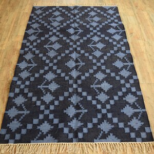 Puede incluir: Una alfombra azul y negra con estampado y borde de flecos. La alfombra tiene un dise&ntilde;o geom&eacute;trico con un patr&oacute;n repetitivo de diamantes y flechas.