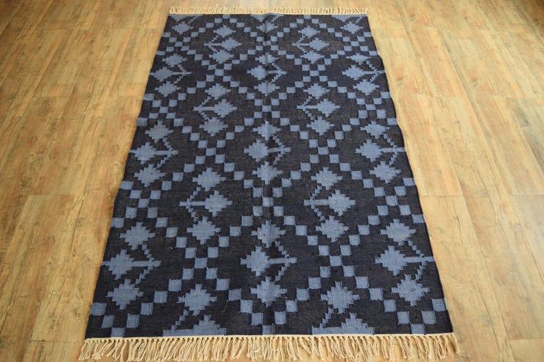 Puede incluir: Una alfombra azul y negra con estampado y borde de flecos. La alfombra tiene un dise&ntilde;o geom&eacute;trico con un patr&oacute;n repetitivo de diamantes y flechas.