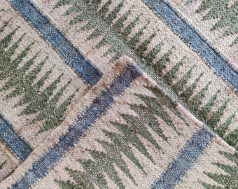Puede incluir: Primer plano de una alfombra tejida con un patrón geométrico en tonos de verde, azul y beige. La alfombra tiene una superficie texturizada y un diseño a rayas.