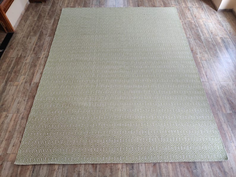 May include: A green and white patterned rug with a geometric design. The rug is made of a woven material and has a soft texture.