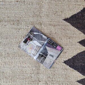 K&ouml;nnte beinhalten: Ein beige-schwarzer Teppich mit einem Magazin darauf. Das Magazin ist auf einer Seite mit dem Text "NV Magazine" und "Style Libre" ge&ouml;ffnet.