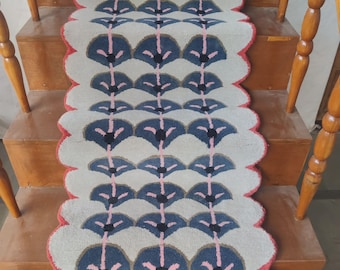 Puede incluir: Una alfombra de pasillo para escaleras con un patrón floral repetido en azul, rosa y negro sobre un fondo crema. Los bordes están festoneados y ribeteados en rojo. La alfombra está colocada en escaleras de madera.