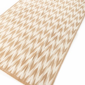 Puede incluir: Una alfombra beige y blanca con un dise&ntilde;o de chevron. La alfombra est&aacute; hecha de un material tejido y tiene un brillo sutil.