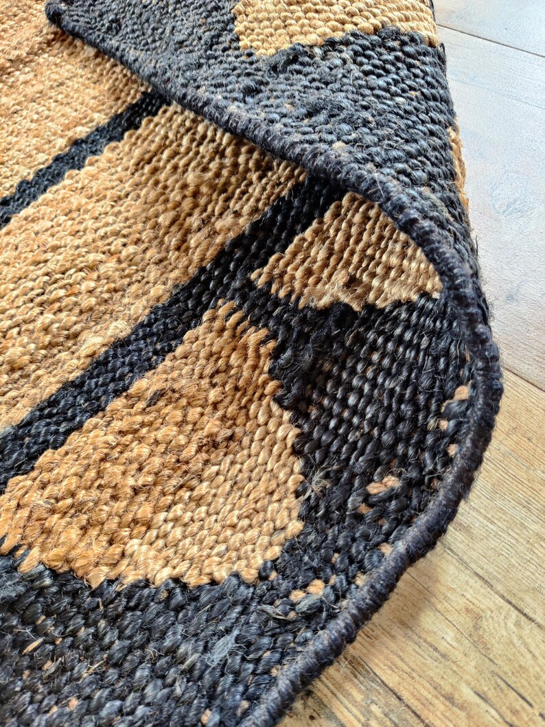 May include: Close-up of a woven jute rug with black stripes. The rug has a natural, earthy texture and is made of natural fibers.